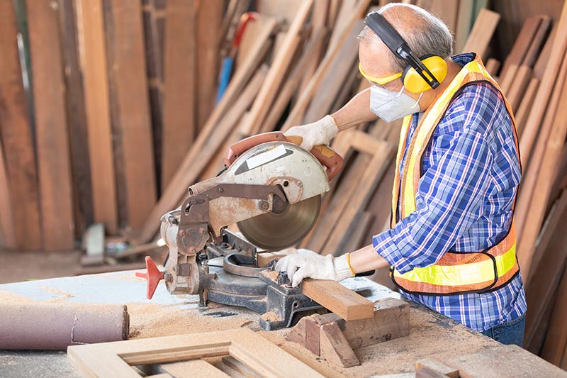 Menuisier coupant du bois et équipé de protection individuelle - - © Istock